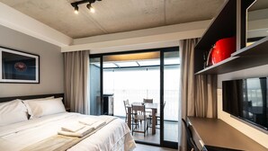 Habitación de hotel con cama, escritorio, silla, televisión y balcón con mesa y sillas.