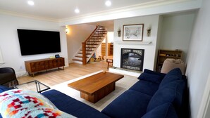 A living room with a TV, sofa, coffee table, fireplace, and staircase. - Family Seattle Stay • Swim Spa • Fire Pit • 9 beds (Woodinville)