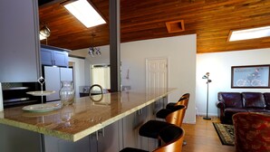 A modern kitchen with a bar area, wooden ceiling, and a living room with a sofa and a framed picture. - Family Seattle Stay • Swim Spa • Fire Pit • 9 beds (Woodinville)