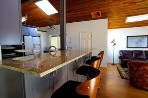 Eine moderne Küche mit Barbereich, Holzboden und einem Wohnzimmer mit Sofa und einem gerahmten Bild.
