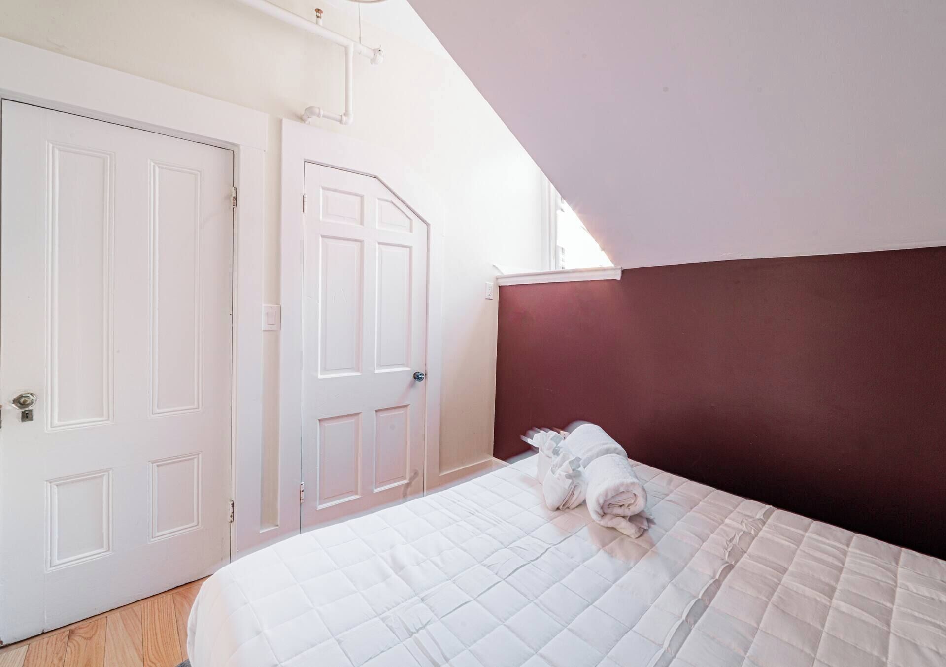 A bedroom with a bed, white walls, a red accent wall, and two white doors.