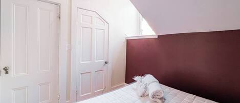 A bedroom with a bed, white walls, a red accent wall, and two white doors.