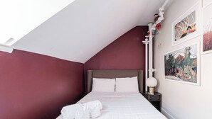 En pænt redt seng med hvide sengetæpper, en sengegavl og et natbord med en lampe.