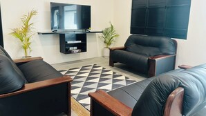 A living room with a flat-screen TV, two leather sofas, a coffee table, and two potted plants. - Villa Vonu - 2 Bedroom Ensuit. Your own pool, secured landscape near the beach. (Pacific Harbour)