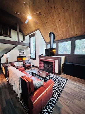 A cozy living room with a fireplace, leather sofa, and a ceiling fan. - Blue Bear Haus - biking/hiking trails from condo, walking distance ski resort (Stateline)