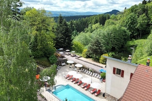 Un espace piscine doté de chaises longues et de parasols, entouré d’une végétation luxuriante et offrant une vue sur la montagne.