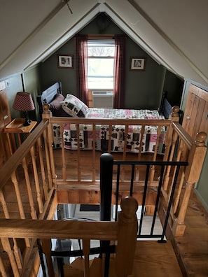 Une chambre à coucher avec un lit, une fenêtre avec des rideaux, un escalier en bois et une vue sur l’extérieur.