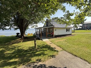 A lakeside cabin with a deck, outdoor seating, and a view of the water.