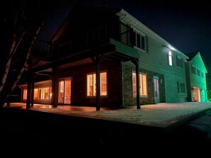 Een huis met twee verdiepingen, voorzien van een overdekte veranda en een exterieur dat in het groen is verlicht.