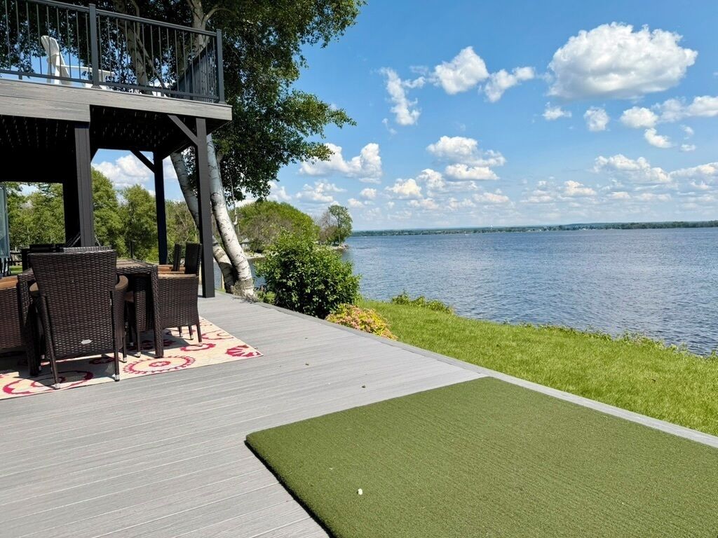 A deck with outdoor furniture, a grassy area, and a view of a body of water.