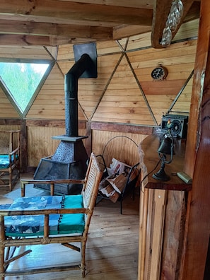 A cozy cabin interior with a wood-burning stove, a chair with a cushion, and a rustic wooden floor. - Cabañas plaza de curacautin (Curacautin)