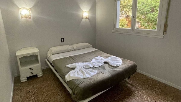 Quarto com cama, mesas de cabeceira, janela e vista para o verde lá fora.