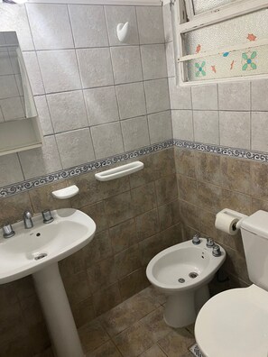 A bathroom with a sink, bidet, toilet, and decorative tiles.