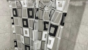 Casa de banho com cortina de chuveiro estampada com padrão geométrico, sanita e chão em mosaico.