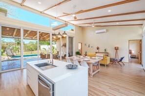 Eine moderne Küche mit einer großen Kochinsel, einem Essbereich mit gelber Couch und Blick auf einen Swimmingpool.