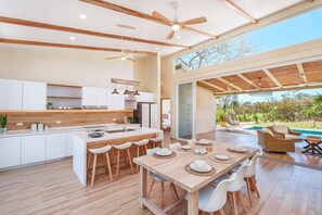 Eine moderne Küche mit Holzschnitzereien, einer zentralen Kochinsel und einem Essbereich mit Blick auf einen Pool.