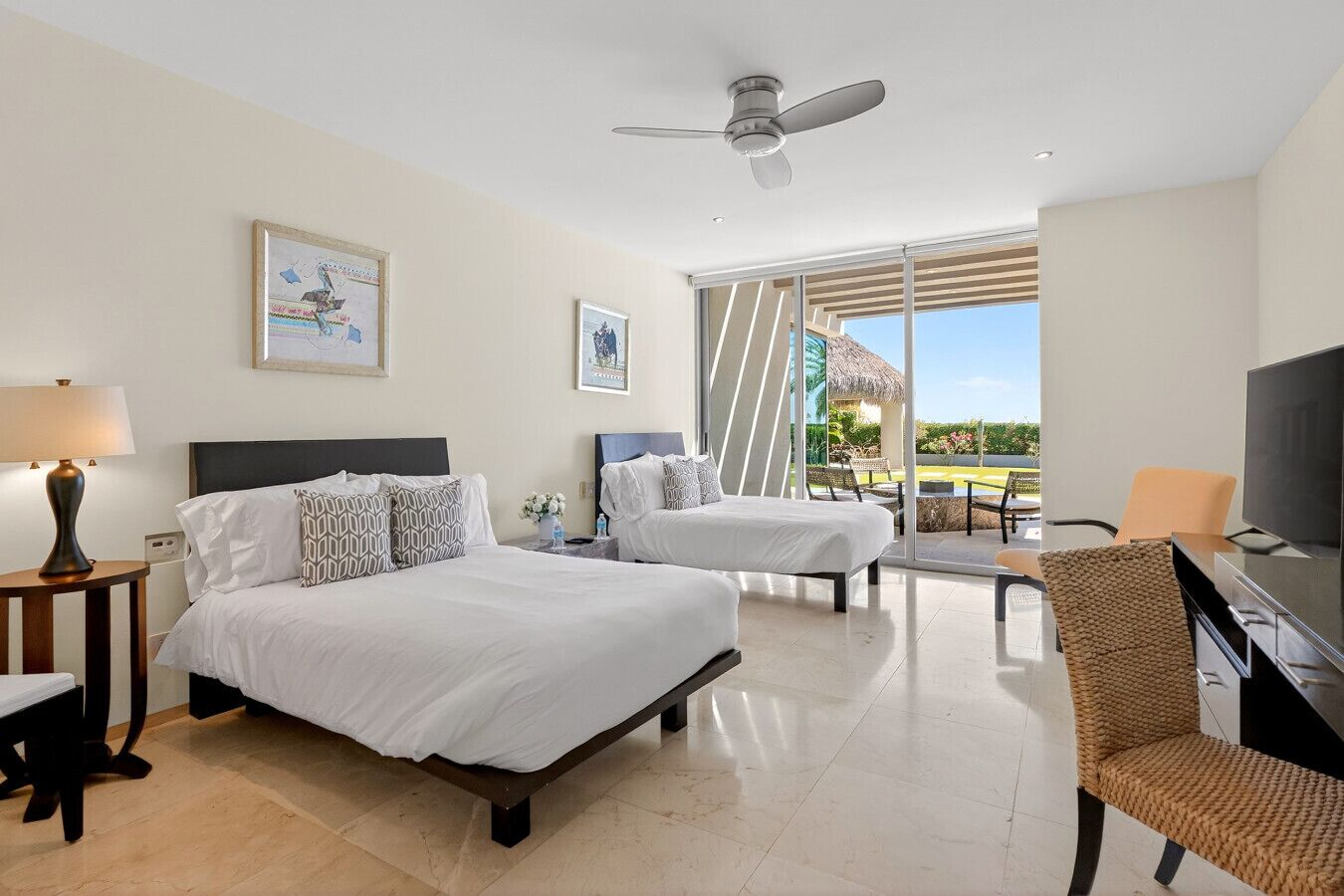 A hotel room with two beds, a TV, a ceiling fan, and a balcony with a view.