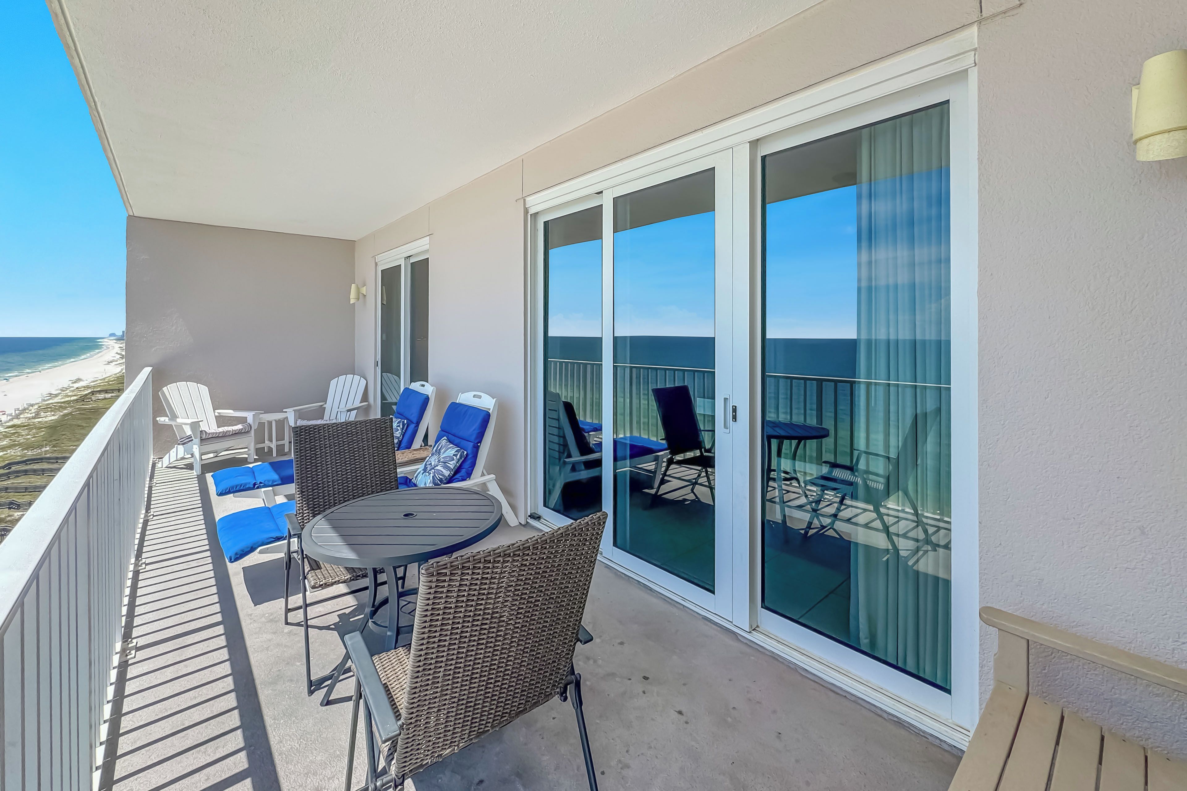 A balcony with a table and chairs, a view of the beach, and a glass door leading to the outdoor area.