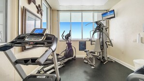 A gym with a treadmill, elliptical, and weight machines, large windows, and a motivational poster. - Windemere 1103 | Beachfront | Seasonally Heated Pool | My Beach Getaways (Pensacola)