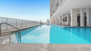 A swimming pool with a metal railing, a clear blue sky, and a building with multiple balconies. - Windemere 1103 | Beachfront | Seasonally Heated Pool | My Beach Getaways (Pensacola)