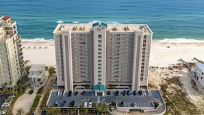 A high-rise hotel with a central tower, parking lot, and beach view. - Windemere 1103 | Beachfront | Seasonally Heated Pool | My Beach Getaways (Pensacola)