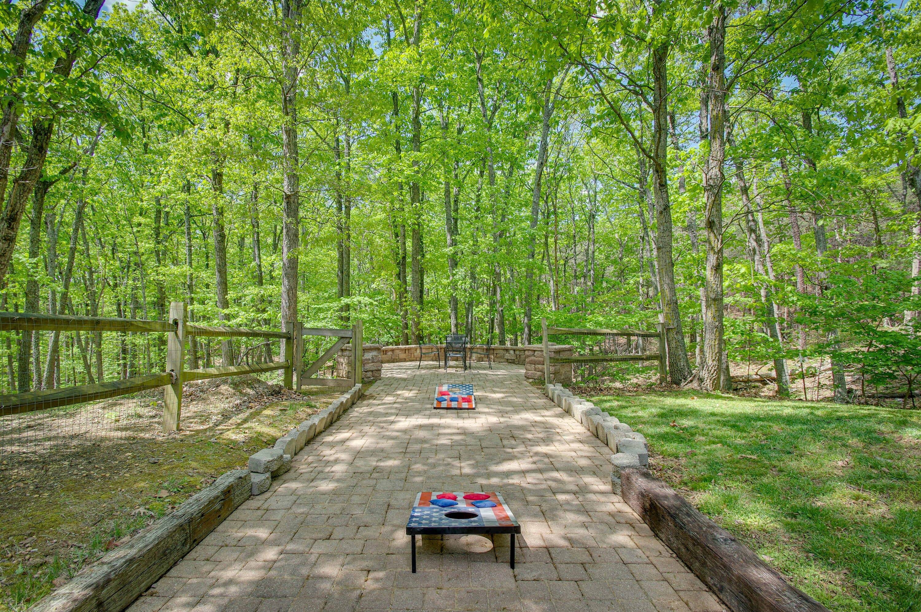A paved pathway in a forested area with a picnic table and a wooden fence.