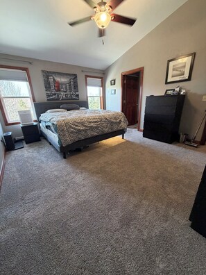 Ein Schlafzimmer mit Bett, Deckenventilator, Fenster, Tür und Kommode.