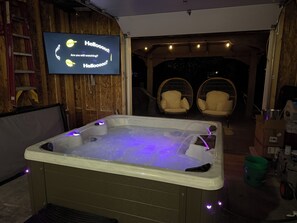 Ein Whirlpool mit LED-Beleuchtung, zwei Korbstühle, ein Fernseher, der eine Meldung anzeigt, und eine Holzverkleidung.
