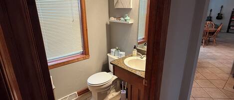 A bathroom with a toilet, sink, and window with blinds.