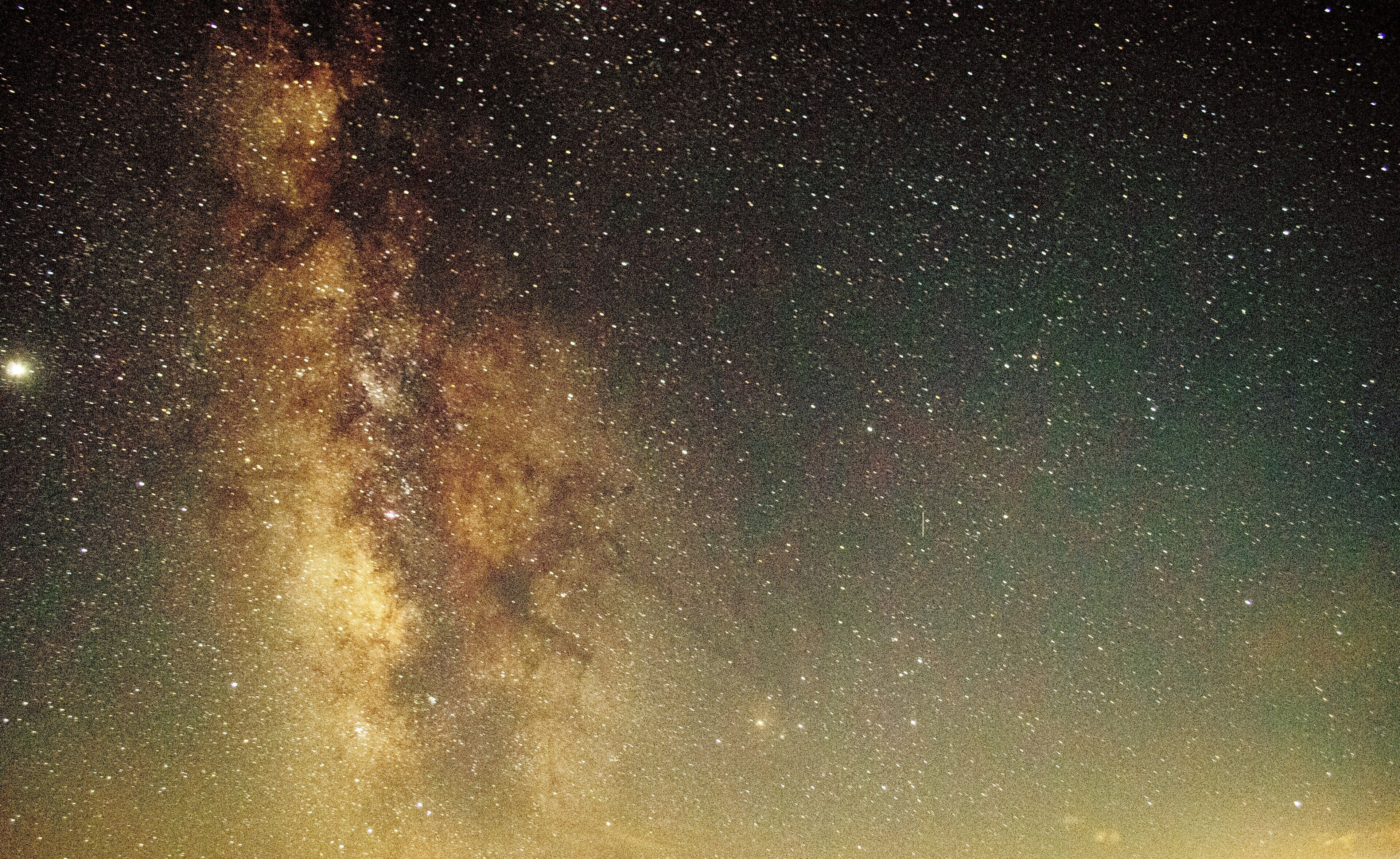 Cielo nocturno estrellado con un denso cúmulo de estrellas y una nebulosa brillante y resplandeciente.