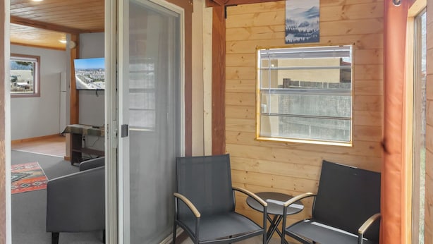 A wooden interior with a sliding glass door leading to a balcony, two chairs, a small table, and a mounted television.
