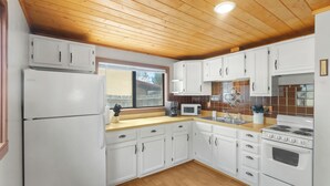 A kitchen with white cabinets, a refrigerator, a microwave, a stove, and a window.