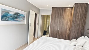 Une chambre à coucher avec un grand lit, une armoire, une porte donnant sur une salle de bain et un tableau encadré au mur.