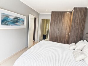 Ein Schlafzimmer mit einem großen Bett, einem Kleiderschrank, einer Tür zu einem Badezimmer und einem gerahmten Bild an der Wand.