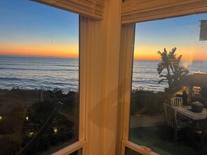 Ein Zimmer mit Meerblick bei Sonnenuntergang, ein Fenster und ein Tisch mit Stühlen.