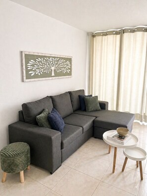 Ein modernes Wohnzimmer mit einem Ecksofa, einem kleinen runden Tisch und passendem Hocker.