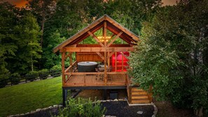 Eine Holzhütte mit Whirlpool, Sitzgelegenheit im Freien und einer Terrasse, umgeben von Bäumen.