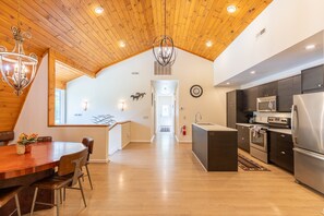 A spacious kitchen with modern appliances, a dining area with a wooden table, and a lofted ceiling with exposed beams. - The Red Barn at Tiffany's Estate - Hot Tub, Pond, Kayaks, Game Room, and much more! (Elk Park)