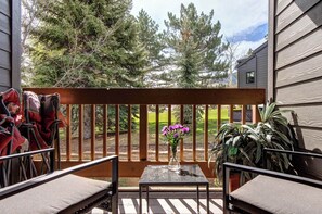 Eine Terrasse mit Tisch, Stühlen, einem Blumenvasen und Blick auf Bäume und ein Haus.