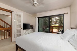 Ein Schlafzimmer mit Bett, Fernseher, einer Schiebetür zum Balkon und einem Deckenventilator.