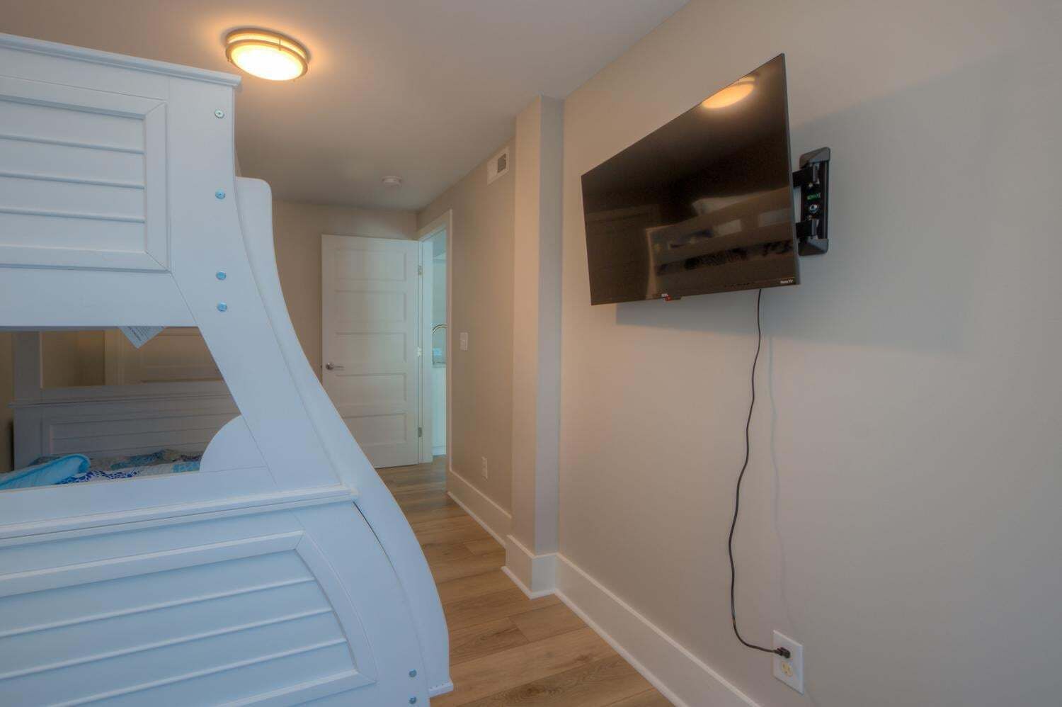 A room with a bunk bed, a mounted TV, and a door leading to another room.