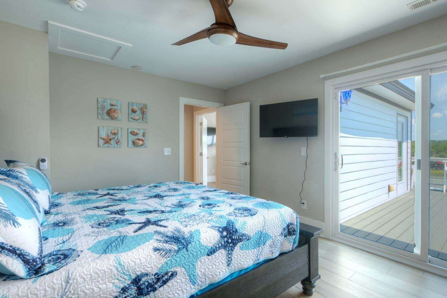 A bedroom with a bed, ceiling fan, artwork, and a TV.