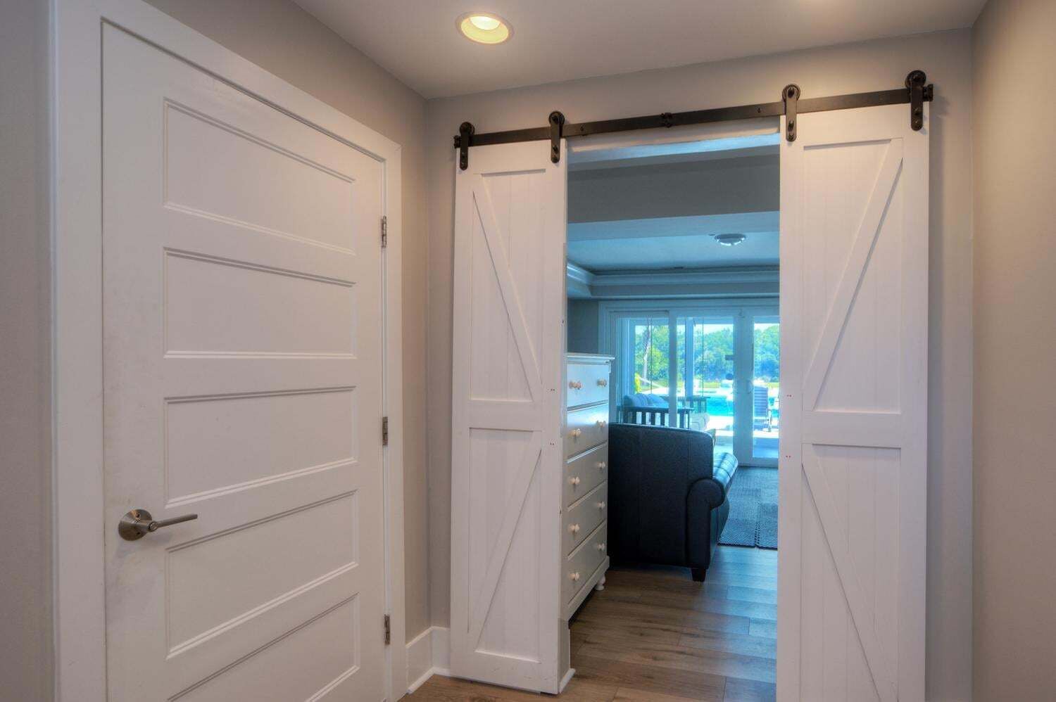 A hallway with a sliding barn door leading to a living area with a pool view.
