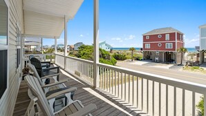 Une terrasse en bois avec des chaises, une table et une vue sur la plage et l’océan.