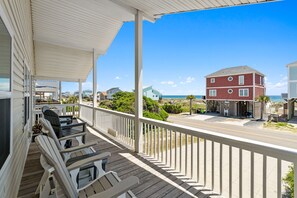 A wooden deck with chairs, a table, and a view of the beach and ocean. - Shout! at the Shore: 4BR/2BA , Ocean Views, perfect for families! (Oak Island)