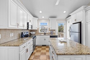 A modern kitchen with white cabinetry, granite countertops, stainless steel appliances, and a view to the outdoors. - Shout! at the Shore: 4BR/2BA , Ocean Views, perfect for families! (Oak Island)