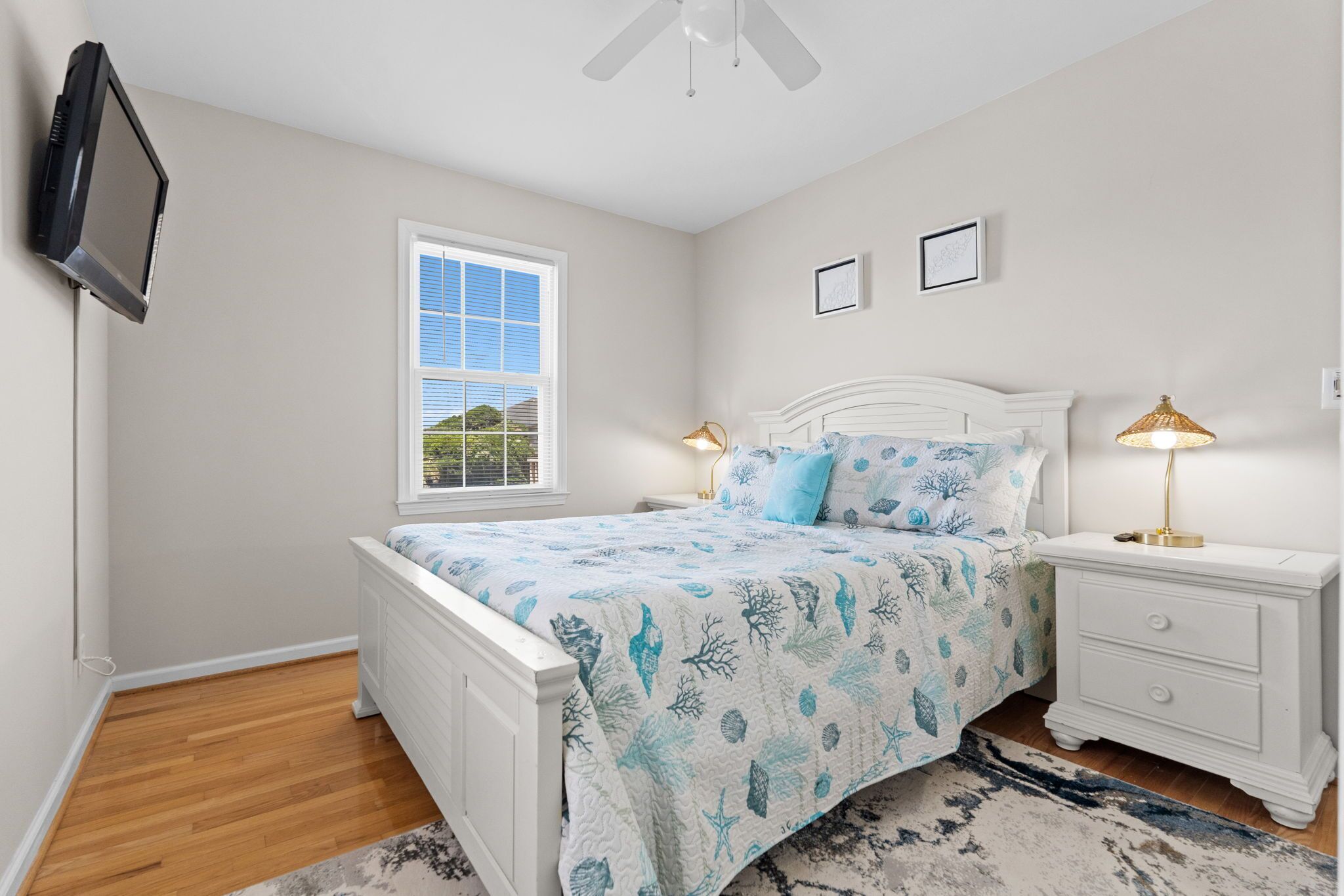 A bedroom with a bed, bedside tables, a TV mounted on the wall, and a window.