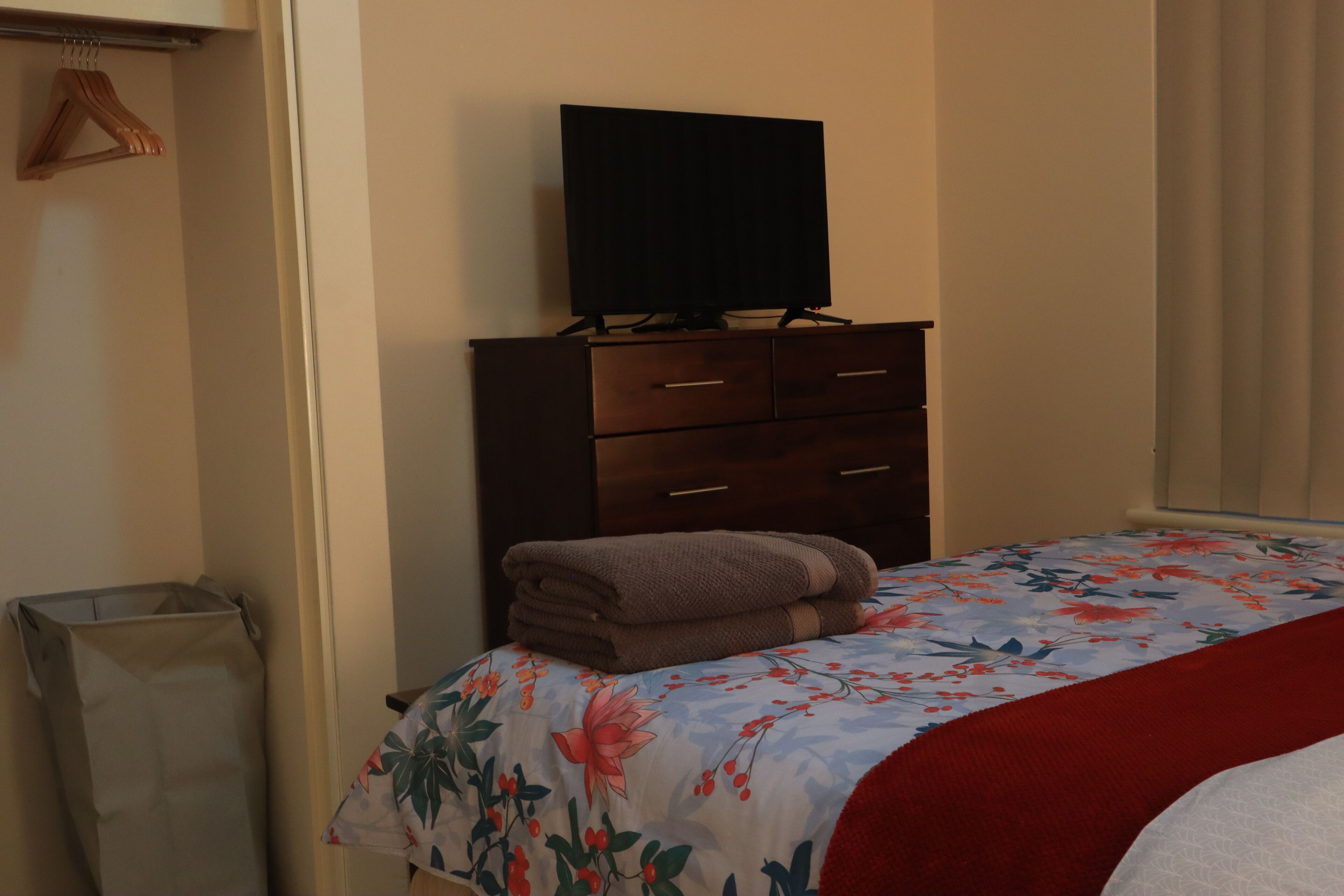 A bedroom with a bed, a dresser, a television, and a window with curtains.