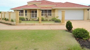 A single-story house with a red-tiled roof, a front garage, and a fenced yard with small shrubs. - Duble Room Near Stunning Beaches in quaint Baldivis (Baldivis)