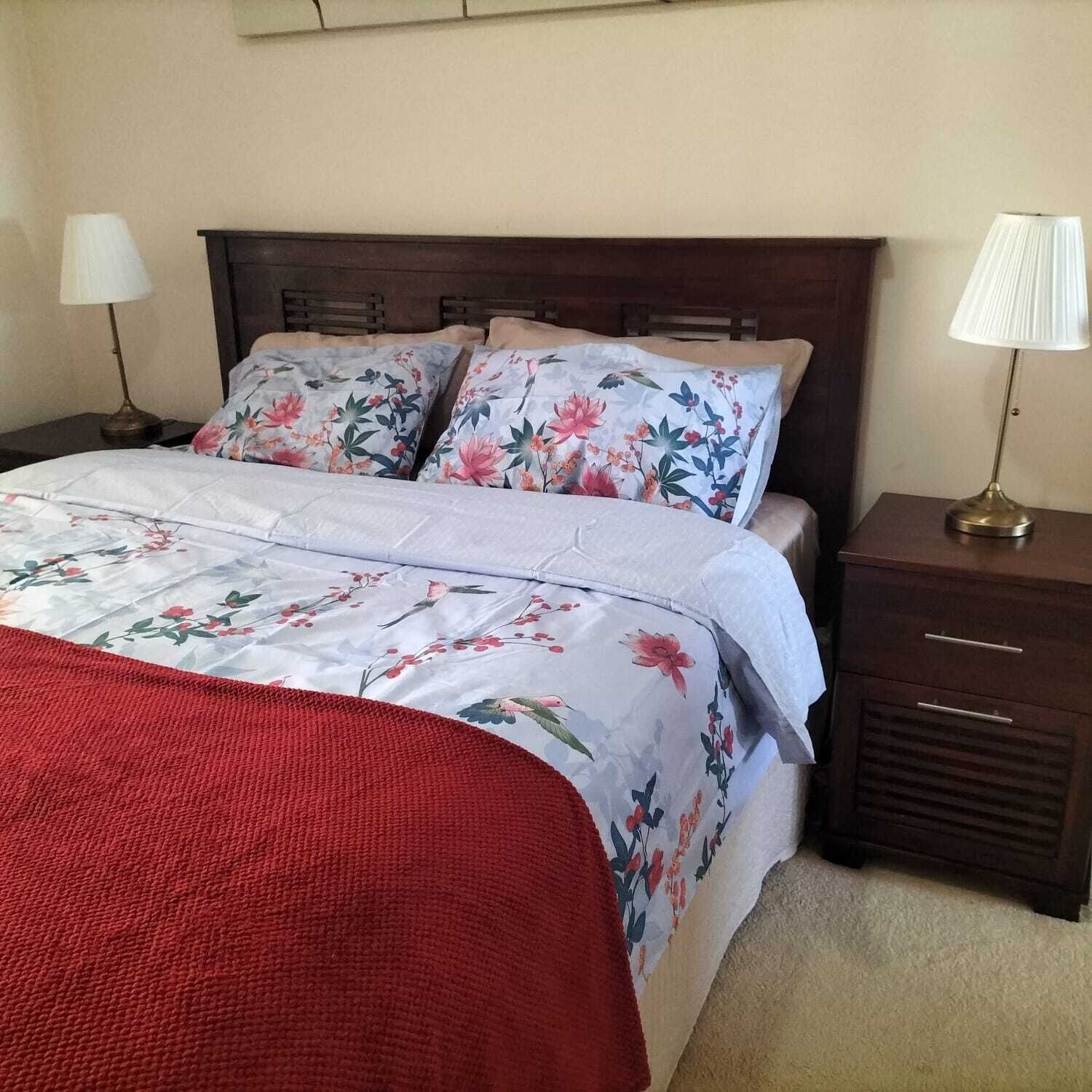A neatly made bed with floral bedding, a red throw blanket, and two bedside lamps on wooden nightstands.